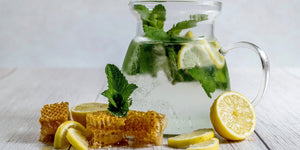 Image of water in a pitcher next to lemons, honey and mint